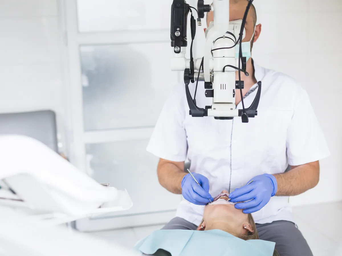 Behandelnder arbeitet an einer Patientin mit einem Dentalmikroskop